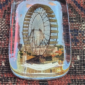 May include: A rectangular glass paperweight featuring an image of the Ferris Wheel from the 1893 World's Fair. The text reads "264 FEET IN DIAMETER". The image is set against a blue sky with clouds.