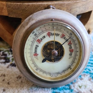 May include: A wooden framed barometer with a white face and black needle. The face has a gold rim and the words "Stormy Rain Change Fair Very Dry" printed around the edge.