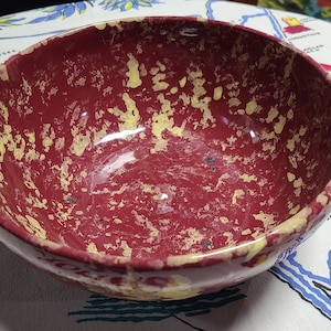 May include: A red and yellow speckled ceramic bowl. The bowl is round and has a smooth, glossy finish.