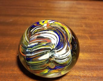 May include: A colorful glass paperweight with swirling patterns of blue, yellow, white, and orange.