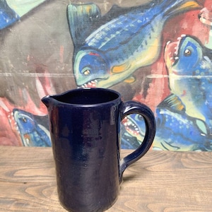 May include: A dark blue ceramic pitcher with a handle. The pitcher is sitting on a wooden surface.