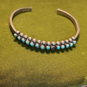 May include: A silver bracelet with turquoise stones set in a row. The bracelet is on a green velvet surface.