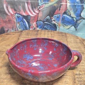 May include: A white ceramic mug with a black handle and the text "But First, Coffee" in a bold, black font. The mug is set against a blurred background, suggesting a cozy setting.