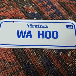 May include: White Virginia license plate with blue lettering that reads "WA HOO" and the number "89" in the top right corner.