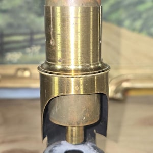 May include: A vintage brass microscope with a black stage and a white powder residue on the stage. The microscope is in focus and the details of the brass are visible.