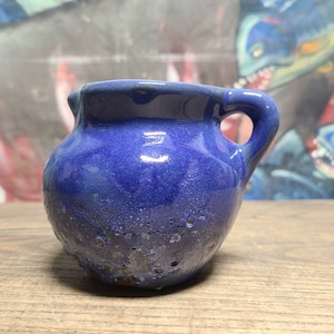 May include: A small, blue ceramic pitcher with a textured surface and a handle. The pitcher is about 4 inches tall and 3 inches wide.
