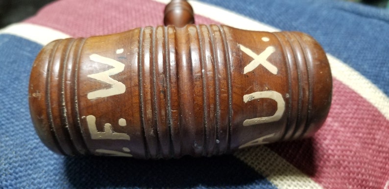 May include: A wooden gavel with white painted letters that read "A.F.W. AUX" on the side. The gavel has a brown finish and is made of wood.