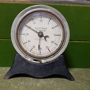 May include: A vintage Eastman Kodak timer with a white face and black hands. The timer has a black base and is set to 30 seconds.