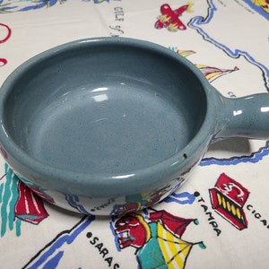 May include: A light blue ceramic bowl with a handle. The bowl is empty and has a speckled glaze.
