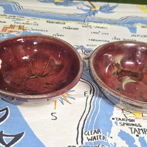 May include: A set of three ceramic mugs with a speckled, cream-colored glaze. Each mug features a different hand-painted floral design in shades of blue, green, and yellow. The mugs have a simple, rounded shape and a comfortable handle.