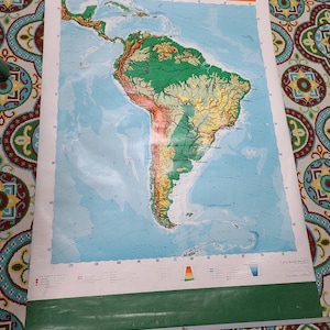 May include: A vintage map of South America with a green, yellow, and brown color scheme. The map shows the continent's physical features, including mountains, rivers, and coastlines. The map is titled "South America" and has a scale bar and legend.