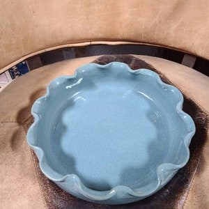 May include: A light blue ceramic bowl with a scalloped edge. The bowl is sitting on a brown leather surface.