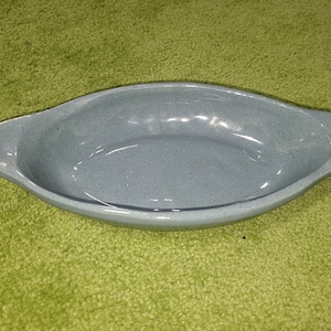 May include: A light blue ceramic oval baking dish with a speckled finish. The dish has two small handles on the sides.