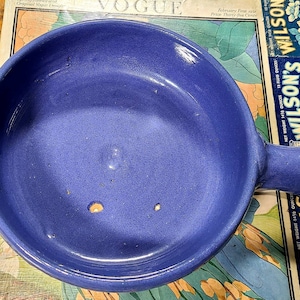 May include: A blue ceramic baking dish with a handle. The dish is round and has a smooth, glazed surface.