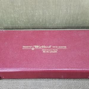 May include: A burgundy rectangular box with the text "TRUBYTE Bioland TRY-ON SELECTOR" in gold lettering. The box is closed and has a textured surface. The box also has the text "Multi-Shade Plastic" and "PAT. NO. 3,015,884".