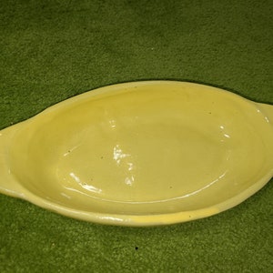 May include: A yellow ceramic baking dish with a rounded oval shape and a smooth, glossy finish.
