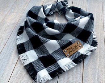 May include: Black and white buffalo plaid dog bandana with frayed edges and a brown leather tag that says "Kitsune Creations".