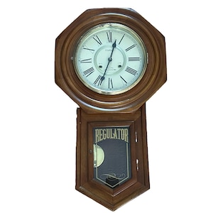 May include: A wooden wall clock with an octagonal top frame and a rectangular lower section. The clock face features Roman numerals, black hands, and the text Waltham 8 Day Clock. The lower glass panel displays the word REGULATOR in gold lettering.