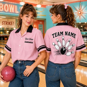 May include: A light pink short-sleeve bowling shirt with a black collar and sleeve stripes. The front features a pocket with the text Your Name. The back displays the text Team Name above a graphic of a black bowling ball hitting white pins.