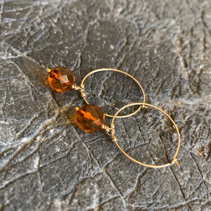 May include: Gold hoop earrings with a small, faceted amber gemstone attached to each hoop.