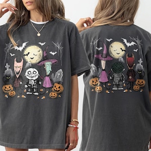 May include: A charcoal gray short-sleeve t-shirt featuring a graphic print of characters from The Nightmare Before Christmas. The design includes Lock, Shock, and Barrel, pumpkins, bats, and a full moon in a graveyard setting on the front and back.