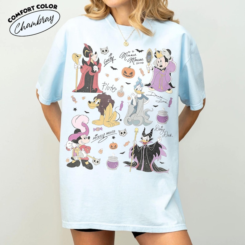 May include: A light blue short-sleeve t-shirt featuring a graphic print of various Disney characters in Halloween costumes, including Mickey Mouse, Minnie Mouse, Donald Duck, Goofy, Pluto, and Daisy Duck, along with small icons like pumpkins and candy.