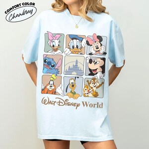 Puede incluir: Una camiseta azul claro con una cuadr&iacute;cula de nueve cuadrados que muestra varios personajes de Disney, incluyendo a Daisy, el Pato Donald, Minnie Mouse, Stitch, Mickey Mouse, Goofy, Pluto, Chip y Chop, y un castillo. El texto Walt Disney World aparece debajo.