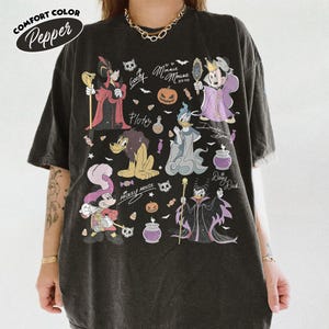 May include: A pepper-colored t-shirt featuring a graphic print of various cartoon characters dressed in Halloween costumes, including pumpkins, candy, and skulls. The text includes names like Goofy, Minnie Mouse, Pluto, Donald Duck, Daisy Duck, and Mickey Mouse.
