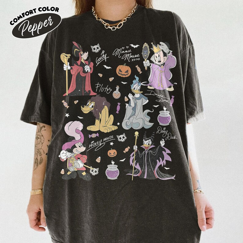 May include: A pepper-colored t-shirt featuring a graphic print of various cartoon characters dressed in Halloween costumes, including pumpkins, candy, and skulls. The text includes names like Goofy, Minnie Mouse, Pluto, Donald Duck, Daisy Duck, and Mickey Mouse.
