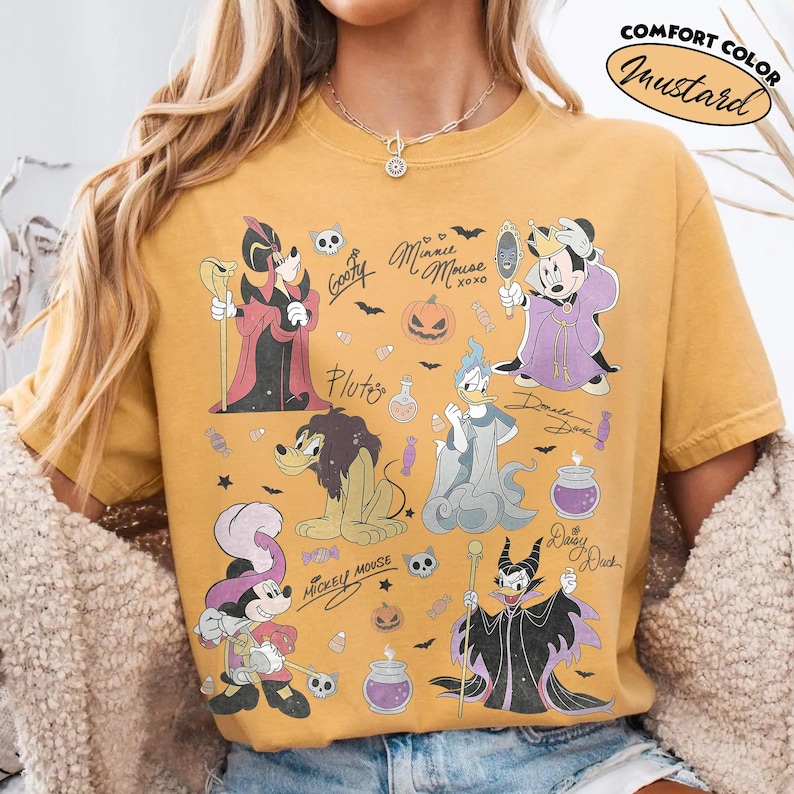 May include: A mustard yellow t-shirt featuring a graphic print of various Disney characters in Halloween costumes, including Mickey Mouse, Minnie Mouse, Donald Duck, and Goofy. The design includes text labels, pumpkins, and candy icons.