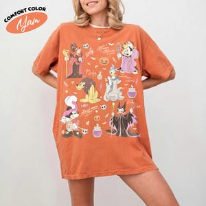 May include: An orange short-sleeve t-shirt featuring a graphic print of various cartoon characters in Halloween costumes, including Mickey Mouse, Minnie Mouse, Pluto, and Donald Duck, along with small icons of pumpkins, candy, and bats.