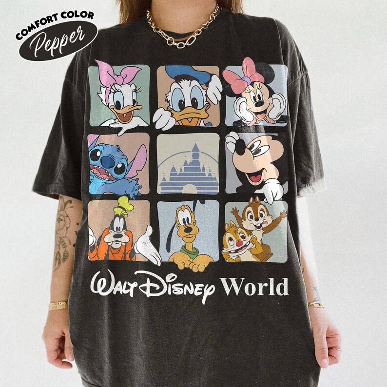 Puede incluir: Una camiseta de manga corta gris carb&oacute;n con una cuadr&iacute;cula de nueve cuadrados que muestra varios personajes de Disney, incluidos Daisy, Donald, Minnie, Stitch, Mickey, Goofy, Pluto, Chip y Dale, y un castillo. El texto Walt Disney World est&aacute; impreso debajo.