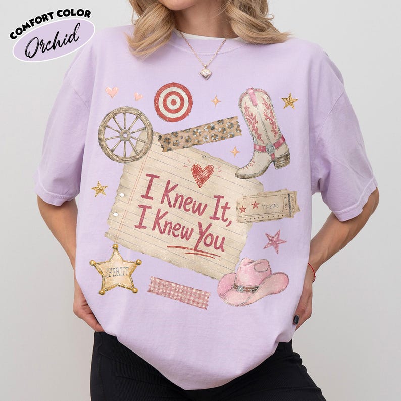 Op de afbeelding: Een orchideekleurig t-shirt met een grafische print van een gelinieerde notitieboekpagina met de tekst I Knew It, I Knew You, omringd door illustraties van een cowboylaars, een roze hoed, een wagenwiel, een sheriffster, een doelwit en sterren.