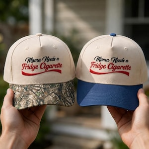 May include: Two five-panel baseball caps with beige crowns and embroidered text that reads Mama Needs a Fridge Cigarette in black and red. One cap features a camouflage print brim, while the other has a solid navy blue brim and top button.