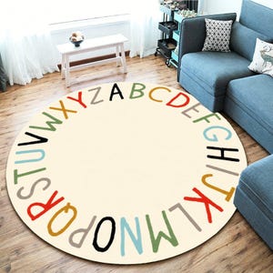 May include: A round area rug with a cream-colored center and a border featuring the alphabet in a circular arrangement. The letters are printed in various colors including red, green, blue, yellow, black, and gray, following the sequence A to Z.
