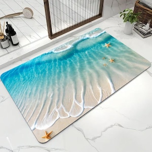 May include: A rectangular bath mat featuring a high-resolution print of a tropical beach shoreline. The design displays turquoise ocean water washing over light beige sand with white sea foam patterns and four orange starfish scattered across.