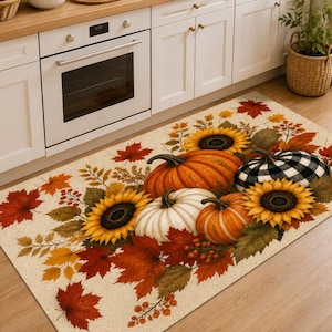 May include: A rectangular kitchen floor mat featuring a seasonal autumn print. The design displays orange, white, and black-and-white buffalo plaid pumpkins, yellow sunflowers, and scattered red and orange maple leaves on a cream-colored background.