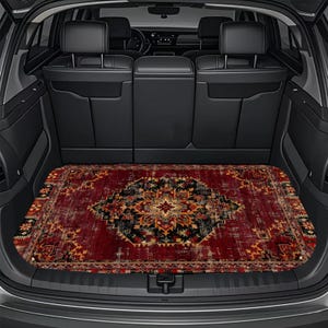 May include: A rectangular car trunk mat featuring a deep red, black, and gold ornate pattern reminiscent of a traditional rug. The mat is fitted into the cargo area of a vehicle with black interior seats and a dark gray trunk lining.