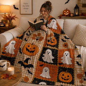 May include: A plush throw blanket featuring a patchwork pattern of Halloween motifs including white ghosts, orange jack-o'-lanterns, black bats, and witch hats, set against a background of black, orange, and tan plaid squares.