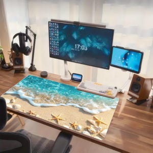 Puede incluir: Una alfombrilla de escritorio rectangular con una impresión de alta resolución de una playa de arena con olas turquesas, espuma de mar blanca y conchas y estrellas de mar dispersas sobre una superficie de escritorio de madera.