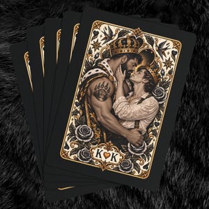 May include: A deck of playing cards featuring a black background and a central illustration of two figures wearing crowns, embracing. The artwork includes gold accents, roses, and birds, with the letters K and K separated by a heart symbol at the bottom.