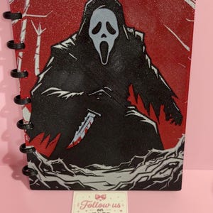 May include: A disc-bound notebook featuring a glittery red and black cover with a graphic of a hooded figure in a white mask holding a knife. Below the notebook is a white card with the text Follow us on INSTAGRAM and @riverasistersprint.