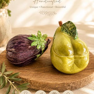 Op de afbeelding: Twee keramische voorraadbussen met deksel in de vorm van groente en fruit. De ene is een dieppaarse aubergine met een groene steel en bladeren, de andere is een felgroene peer met een bruine steel en een groen blad. Beide hebben een glans.