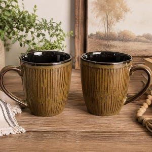 May include: Two ceramic mugs with a dark brown, textured exterior featuring vertical carved lines and a smooth, glossy black interior. Each mug has a curved handle and a wide rim, showcasing a consistent earthy tone and a sturdy, cylindrical shape.