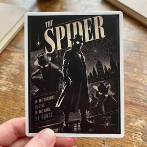 May include: A black and white sticker featuring a comic book illustration of "The Spider." The image shows a figure in a trench coat and fedora, with two other figures in the background. Text includes "In the Shadows, He Sees. In the Dark, He Hunts."