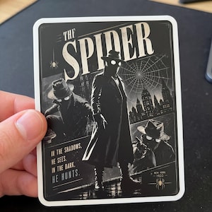 May include: A black and white sticker featuring a vintage comic book style illustration of "The Spider." The image shows a figure in a trench coat and fedora, with the text "In the shadows, he sees. In the dark, he hunts."