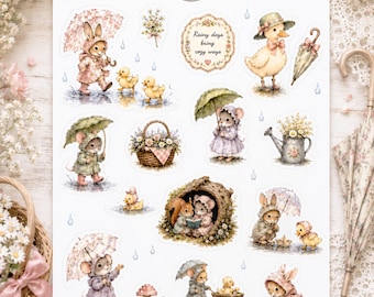 May include: A sticker sheet featuring various illustrations of animals in rain gear, including rabbits, mice, and ducklings with umbrellas. The text reads, "Rainy days bring cozy ways." The sheet includes a basket of flowers, a watering can, and mushrooms, all rendered in a soft, muted colour palette.