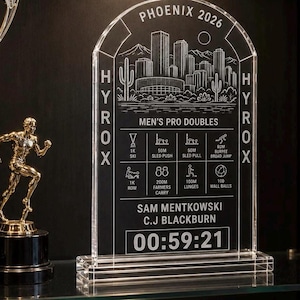 May include: A clear, arched acrylic trophy featuring an etched Phoenix skyline, the text PHOENIX 2026, HYROX, MEN'S PRO DOUBLES, the names SAM MENTKOWSKI and C.J. BLACKBURN, and a race time of 00:59:21, alongside icons for various fitness exercises.
