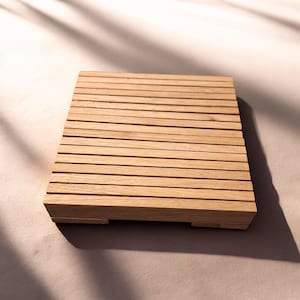 Könnte beinhalten: Ein quadratischer Untersetzer aus Holz, der aus mehreren parallelen, hellbraunen Lamellen besteht. Das Objekt verfügt über eine geriffelte Oberfläche mit sichtbarer Holzmaserung und wird von kleinen, flachen Füßen an den Ecken gestützt.