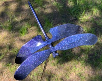 Pode incluir: Uma estaca de jardim de metal azul em forma de libélula com acabamento brilhante. A libélula tem duas pares de asas e um corpo longo e fino.